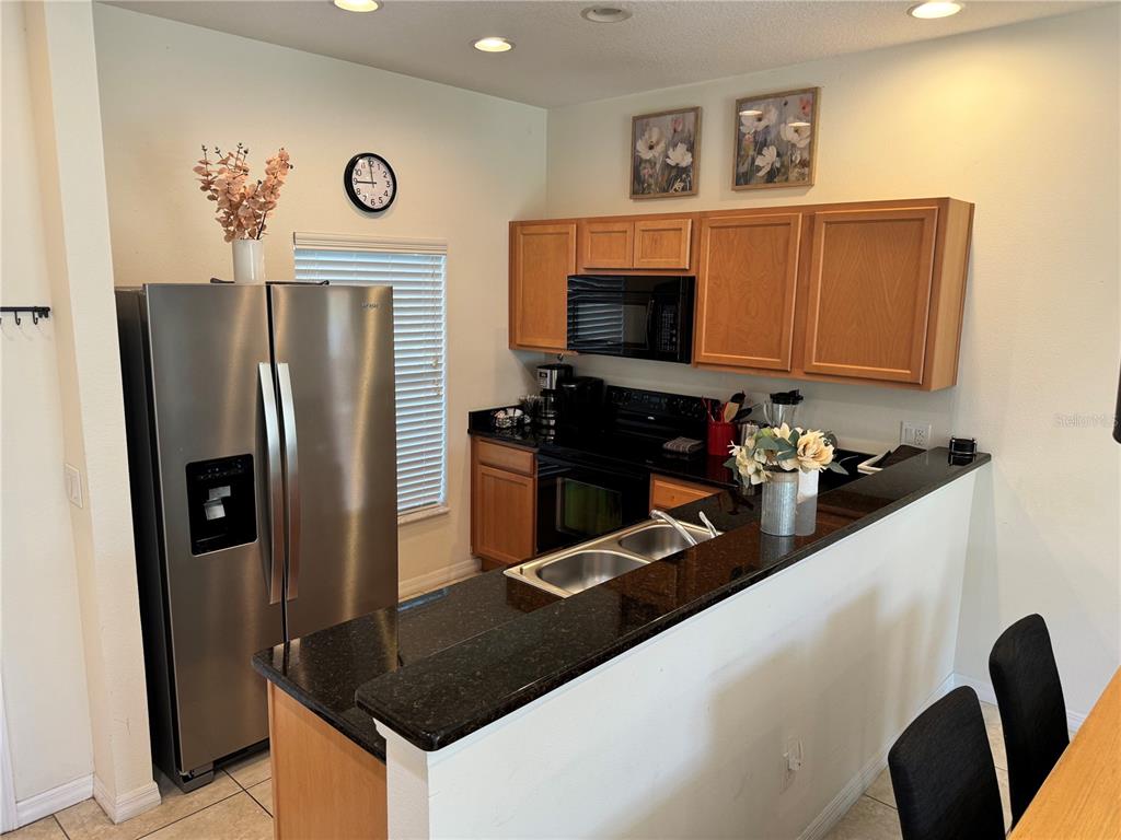 A kitchen features wood cabinets, black countertops, stainless steel appliances, and a breakfast bar — 3003 WHITE ORCHID ROAD, KISSIMMEE, FL