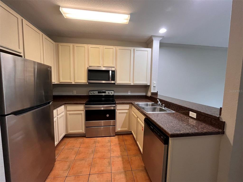 A kitchen features off-white cabinets, stainless steel appliances, dark countertops, and terracotta tile flooring — 14200 AVALON ROAD UNIT 431, WINTER GARDEN, FL