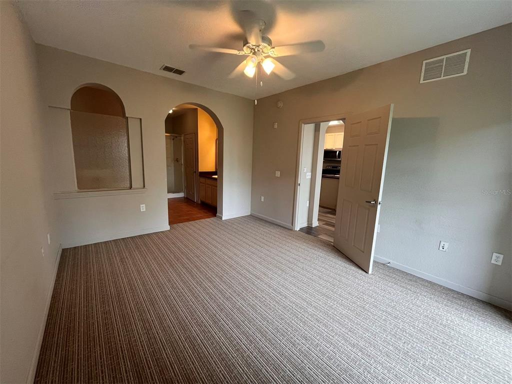 A carpeted bedroom features an arched entryway to a bathroom and an open doorway — 14200 AVALON ROAD UNIT 431, WINTER GARDEN, FL