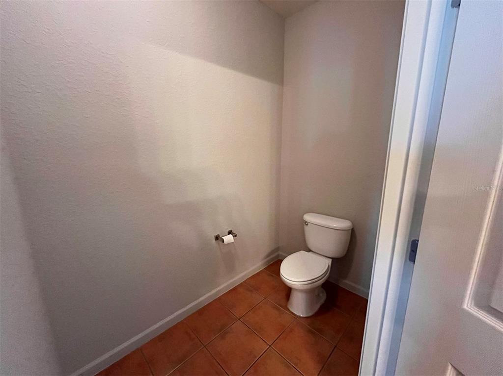 A small bathroom features a white toilet, a toilet paper holder, and brown tile flooring — 14200 AVALON ROAD UNIT 431, WINTER GARDEN, FL
