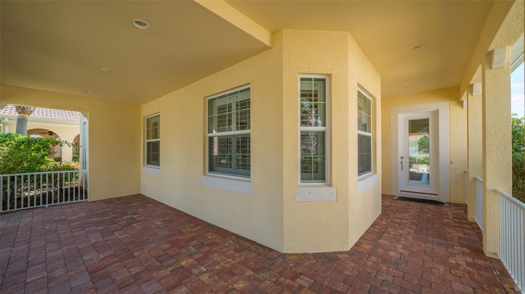 A covered patio with brick pavers, yellow stucco walls, and a white door and railing — 1498 ERNESTO DRIVE, SARASOTA, FL