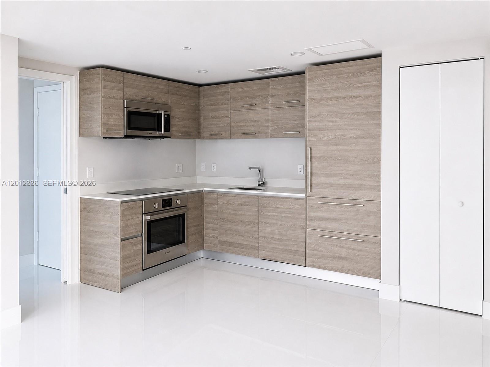 A modern kitchen with wood-grain cabinets and white countertops opens into a bright living area — 1300 S Miami Ave # 4507, Miami FL 33130, MIAMI, FL