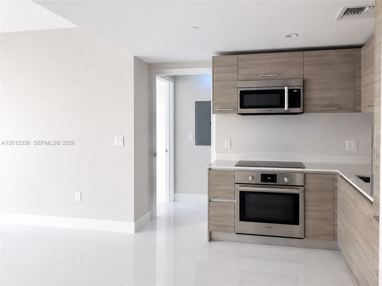 A modern kitchen features wood-grain cabinetry, stainless steel appliances, and white tile flooring — 1300 S Miami Ave # 4507, Miami FL 33130, MIAMI, FL