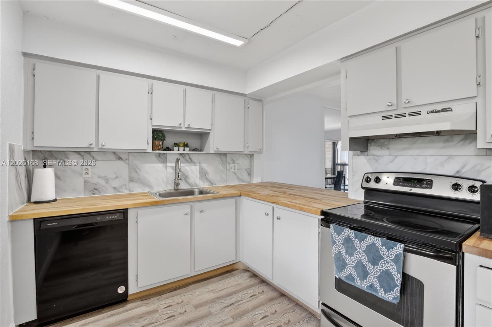 A kitchen features white cabinets, a wood countertop, marble-style backsplash, and black and stainless appliances — 7020 Nova Dr # 308D, Davie FL 33317, DAVIE, FL