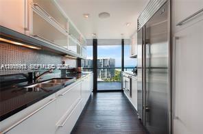 A modern galley kitchen features white cabinetry, dark countertops, and a view of the ocean — 101 20th St # 1907, Miami Beach FL 33139, MIAMI BEACH, FL