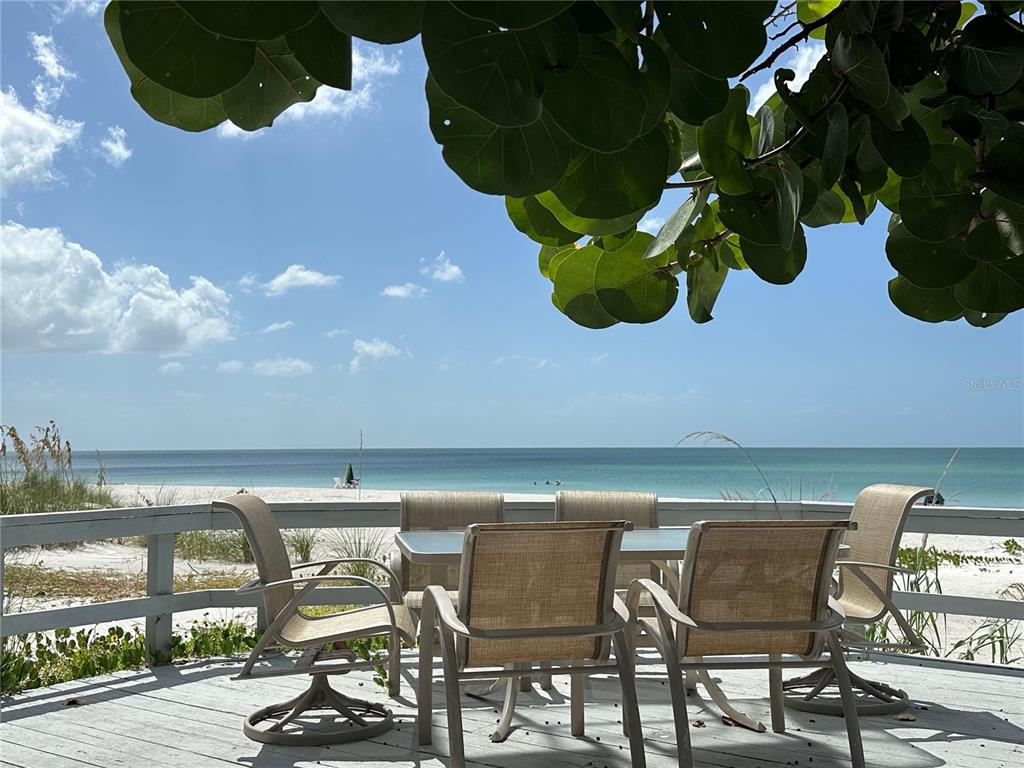 A patio with outdoor furniture overlooks a sandy beach and the ocean under a tree — 2823 GULF OF MEXICO DRIVE, LONGBOAT KEY, FL
