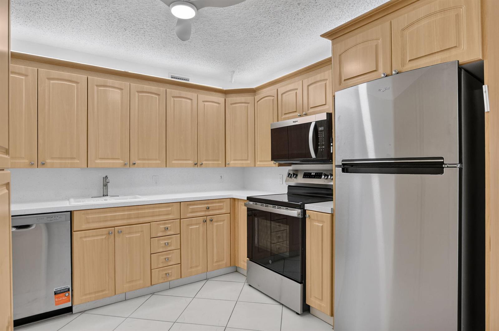 A kitchen featuring light wood cabinets, stainless steel appliances, white countertops, and white tile flooring — 3057 Yarmouth C, Boca Raton FL 33434, BOCA RATON, FL
