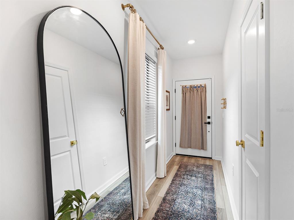 A hallway features a large arched floor mirror, light wood flooring, and a patterned runner — 6524 SILVERSTAR DRIVE, SARASOTA, FL