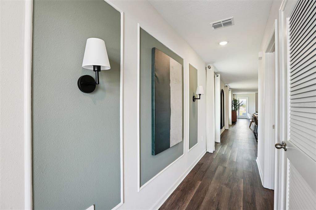A hallway features sage green wall panels with white trim, wall sconces, and wood flooring — 7953 FORREST FOX WAY, LAKELAND, FL