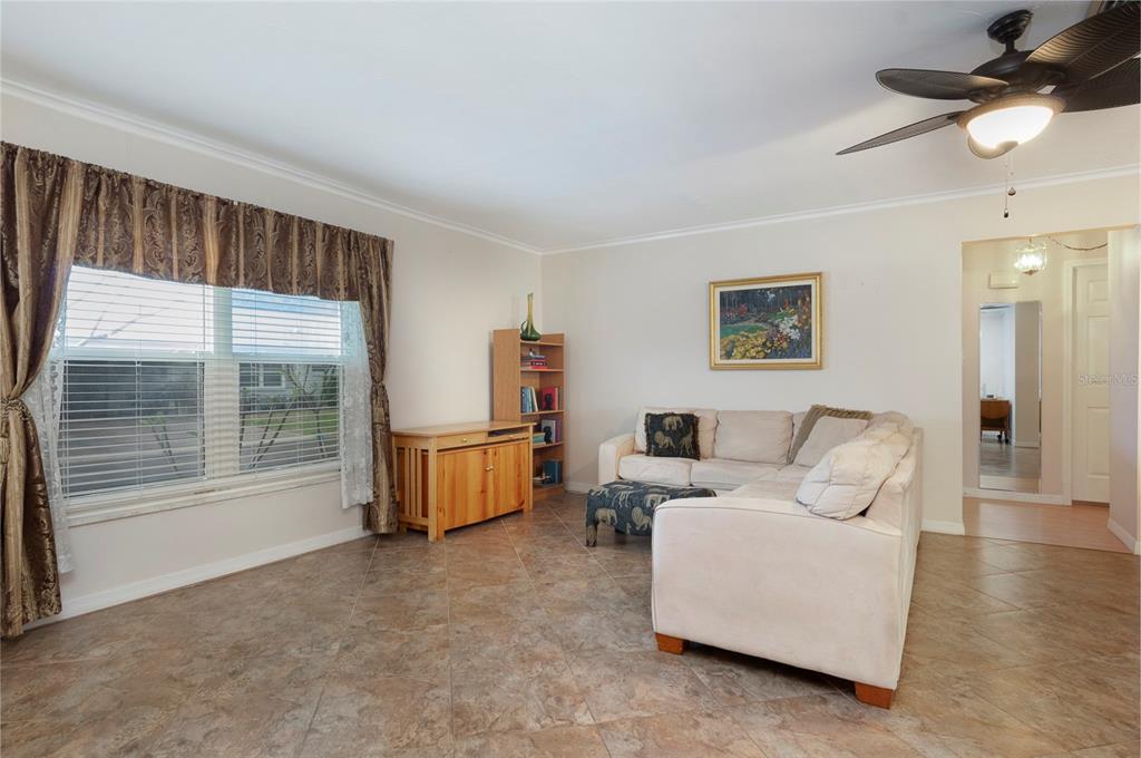 A living room features tile flooring, a beige sectional sofa, a wooden bookshelf, and windows — 8303 ANNWOOD ROAD, SEMINOLE, FL