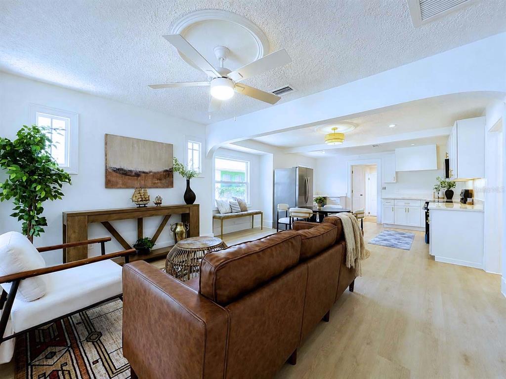 An open-concept living room and kitchen feature a brown leather sofa, wood flooring, and white cabinetry — 1835 24TH STREET S, ST PETERSBURG, FL