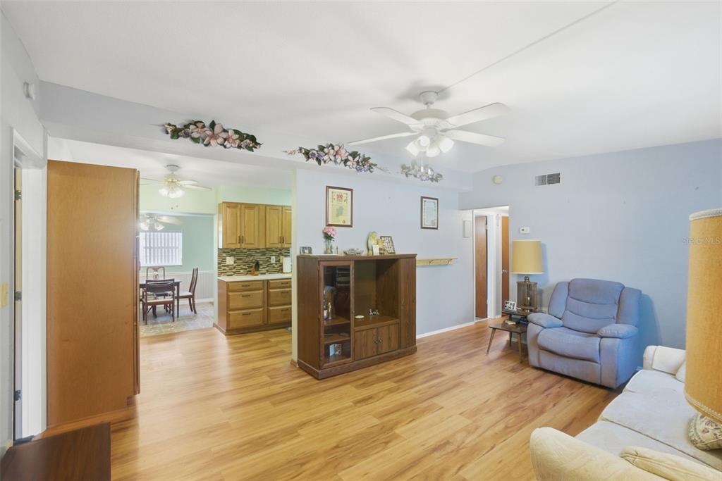 A living room with wood-look flooring leads to an open kitchen with wooden cabinets — 481 KENTIA ROAD, CASSELBERRY, FL