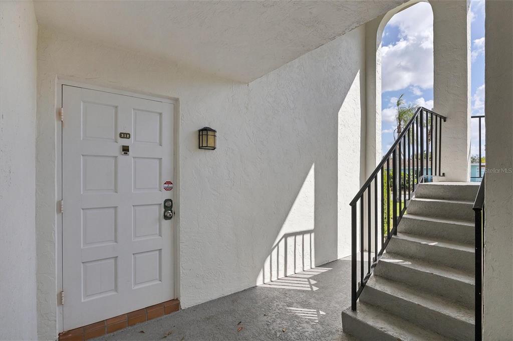 A white door with a number plate sits beside an outdoor staircase with railings — 5800 HOLLYWOOD BOULEVARD UNIT 312, SARASOTA, FL