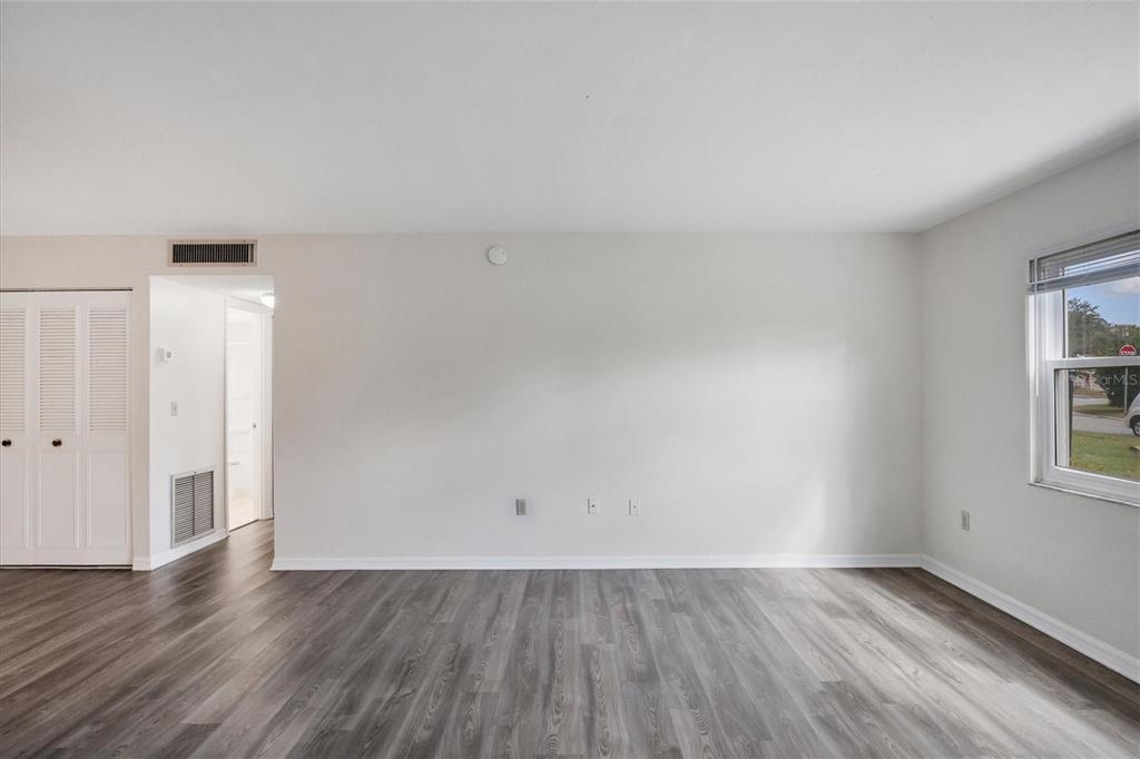 An empty living room features light gray walls, wood-look flooring, and a window with blinds — 5800 HOLLYWOOD BOULEVARD UNIT 312, SARASOTA, FL