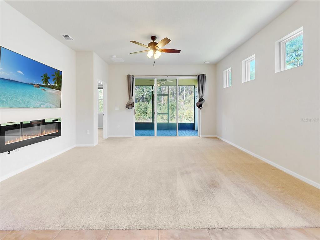 A living room features beige carpeting, a wall-mounted television, a fireplace, and sliding glass doors — 2542 CLIFF WAY, ST CLOUD, FL