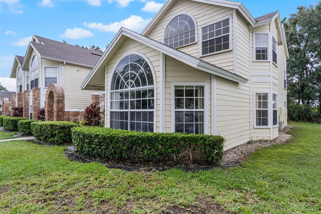 A two-story townhouse with light yellow siding, a large arched window, and manicured hedges — 5017 LAGUNA BAY CIRCLE UNIT 95, KISSIMMEE, FL