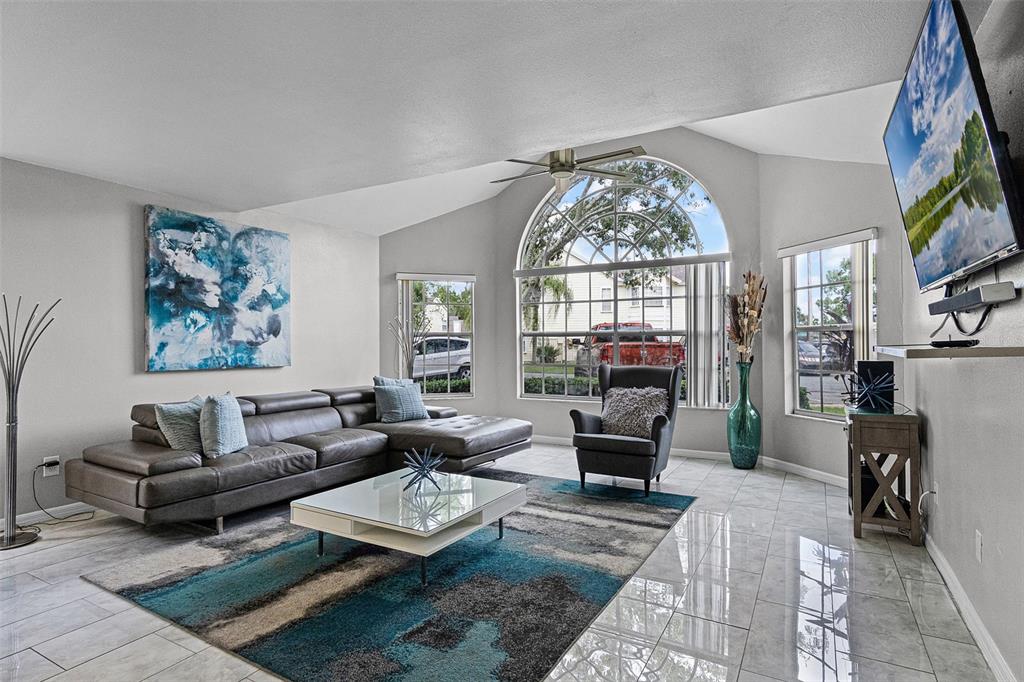 A living room features a vaulted ceiling, a large arched window, and tile flooring — 5017 LAGUNA BAY CIRCLE UNIT 95, KISSIMMEE, FL