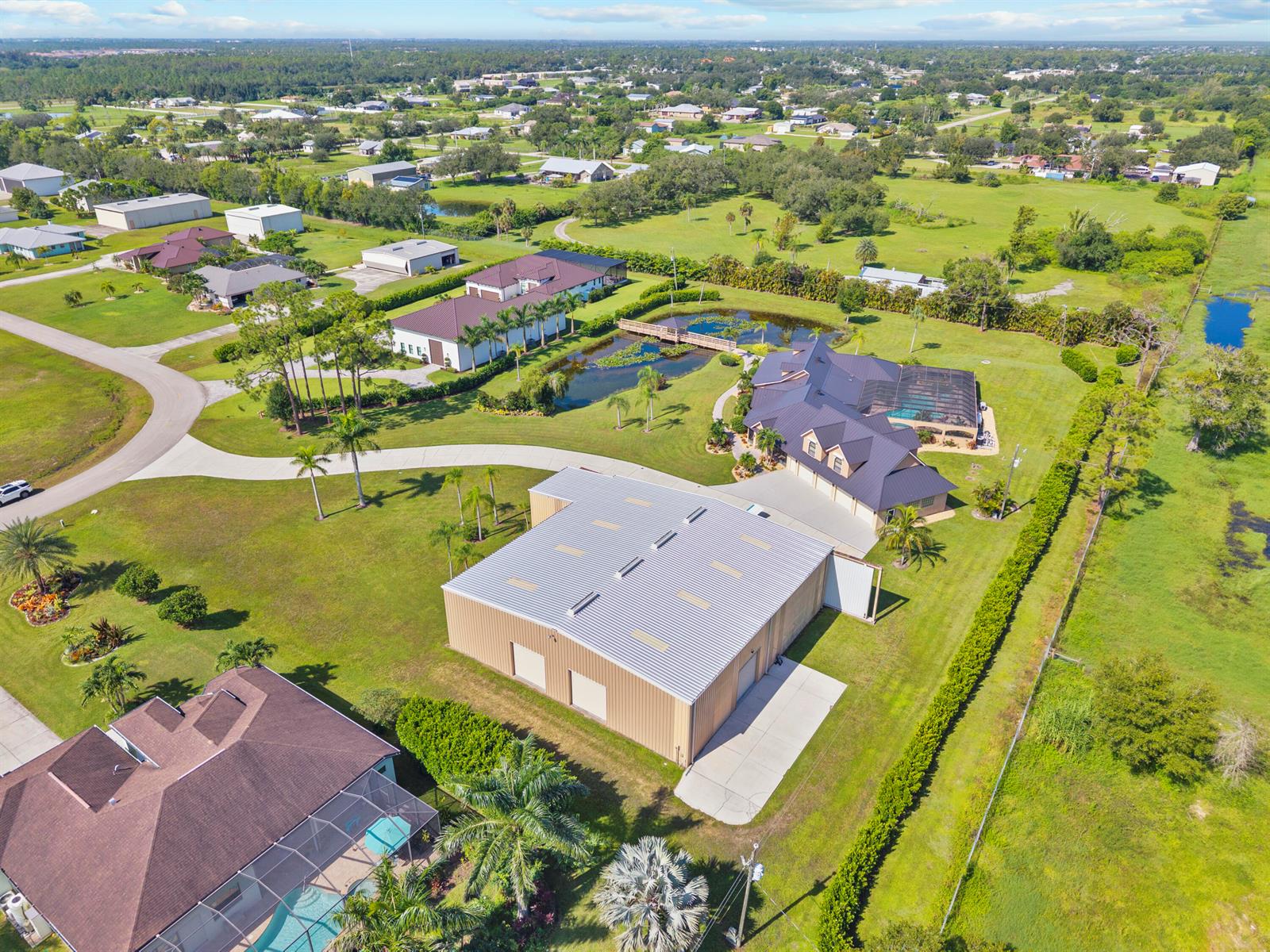 An aerial view shows a large metal workshop, a house with a pool, and ponds — 3561 Downwind Lane, FL 33917, FL