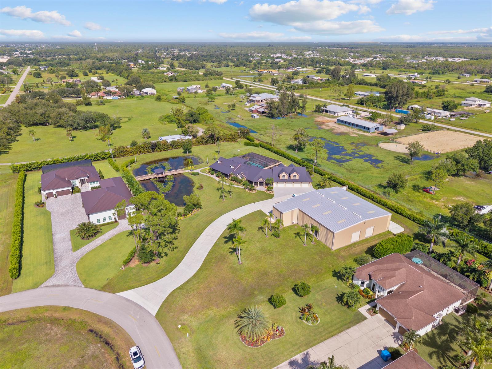 An aerial view shows several houses, a large metal workshop, and a pond with a bridge — 3561 Downwind Lane, FL 33917, FL