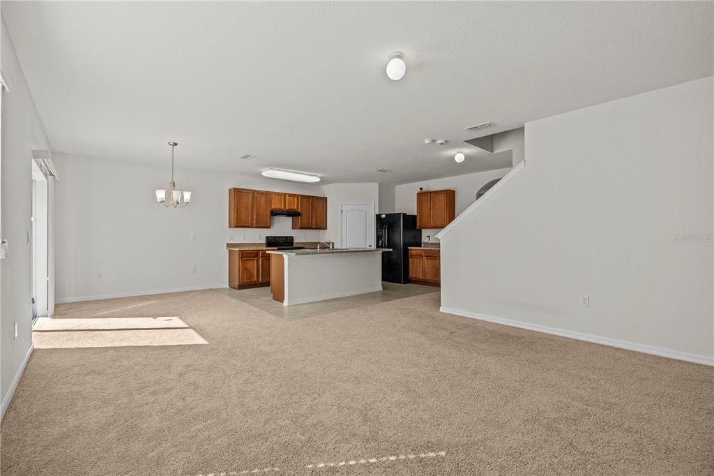 An open-concept living area features beige carpeting, a kitchen with wood cabinets, and an island — 817 SHEEN CIRCLE, HAINES CITY, FL