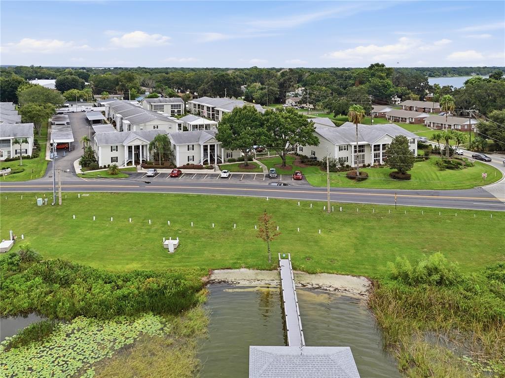 An aerial view shows a multi-story apartment complex across a road from a lake dock — 689 LAKE HOWARD DRIVE NW UNIT 213, WINTER HAVEN, FL