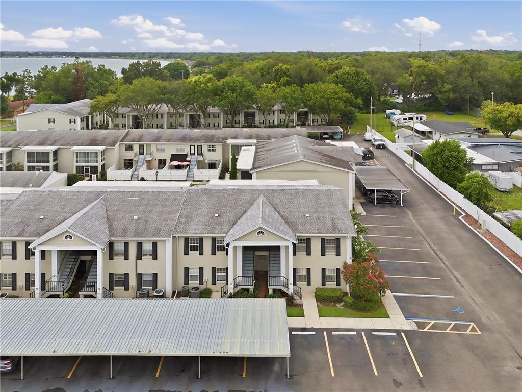 An aerial view shows multi-story apartment buildings with covered parking spaces and a nearby lake — 689 LAKE HOWARD DRIVE NW UNIT 213, WINTER HAVEN, FL
