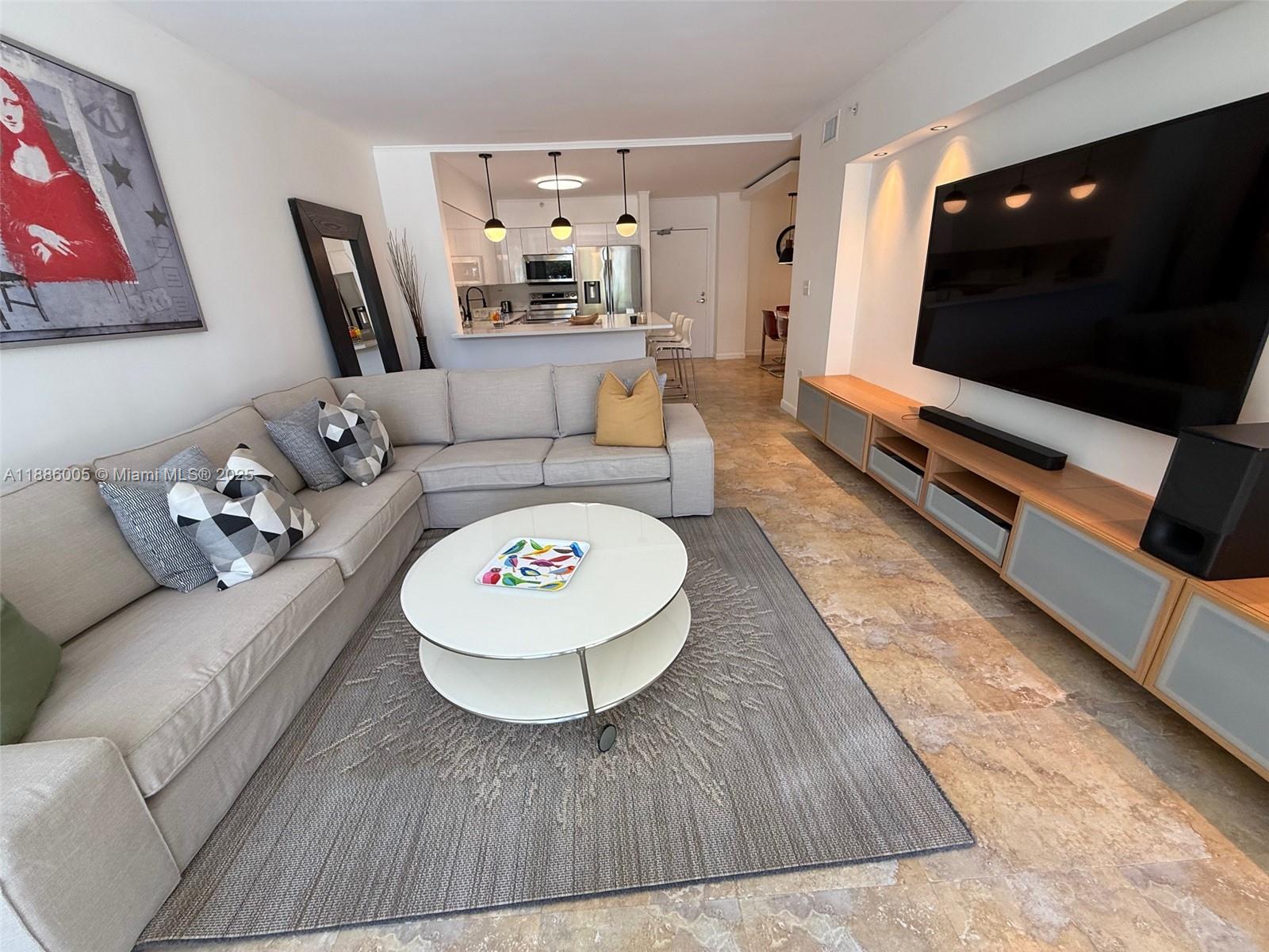 A living room features a large sectional sofa, a round coffee table, and a wall-mounted television — 1500 Bay Rd # 122S, Miami Beach FL 33139, MIAMI BEACH, FL