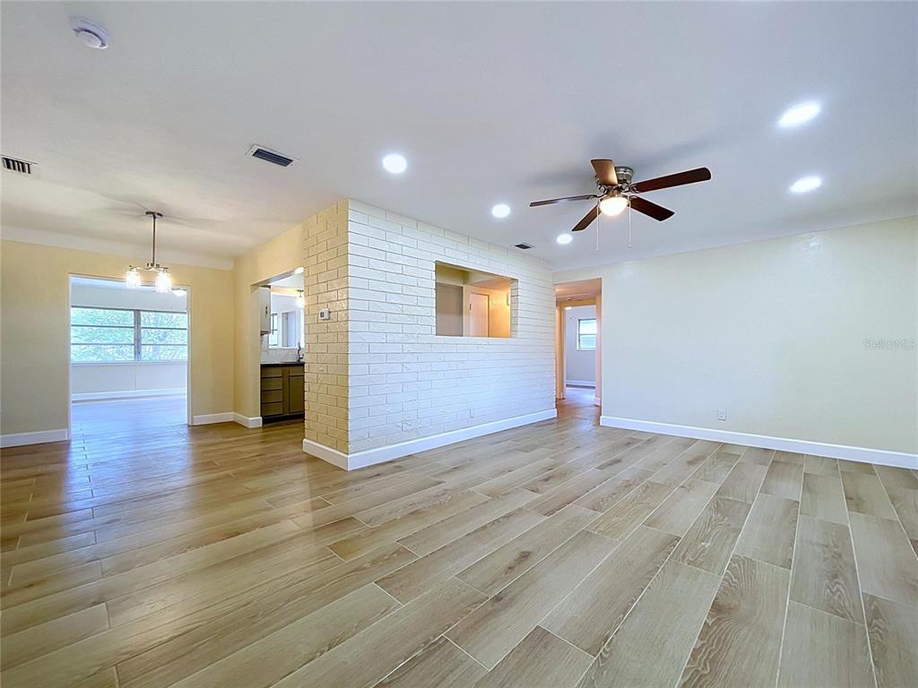 A living room features light wood-look tile flooring, a white brick accent wall, and recessed lighting — 9813 51ST AVENUE N, ST PETERSBURG, FL