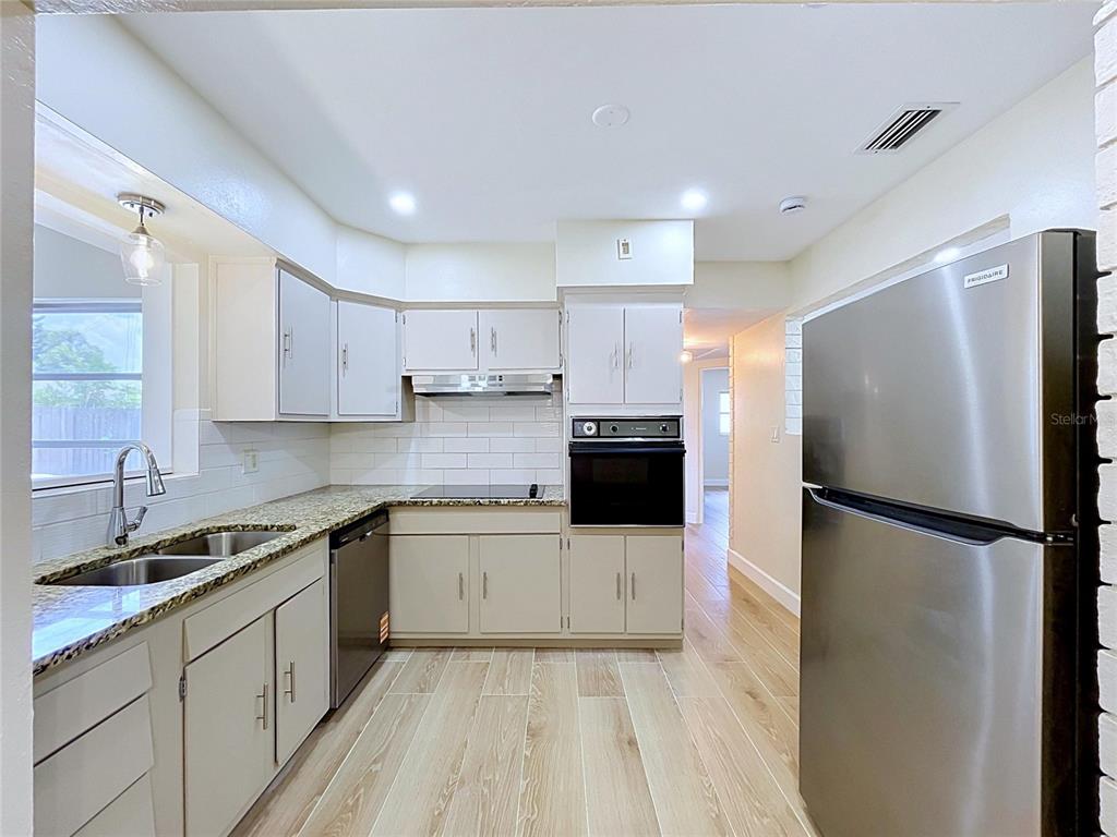 A kitchen features light-colored cabinets, granite countertops, stainless steel appliances, and wood-look tile flooring — 9813 51ST AVENUE N, ST PETERSBURG, FL
