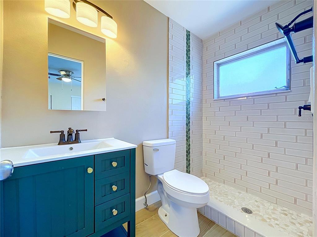 A bathroom features a teal vanity, a white toilet, and a tiled walk-in shower — 9813 51ST AVENUE N, ST PETERSBURG, FL