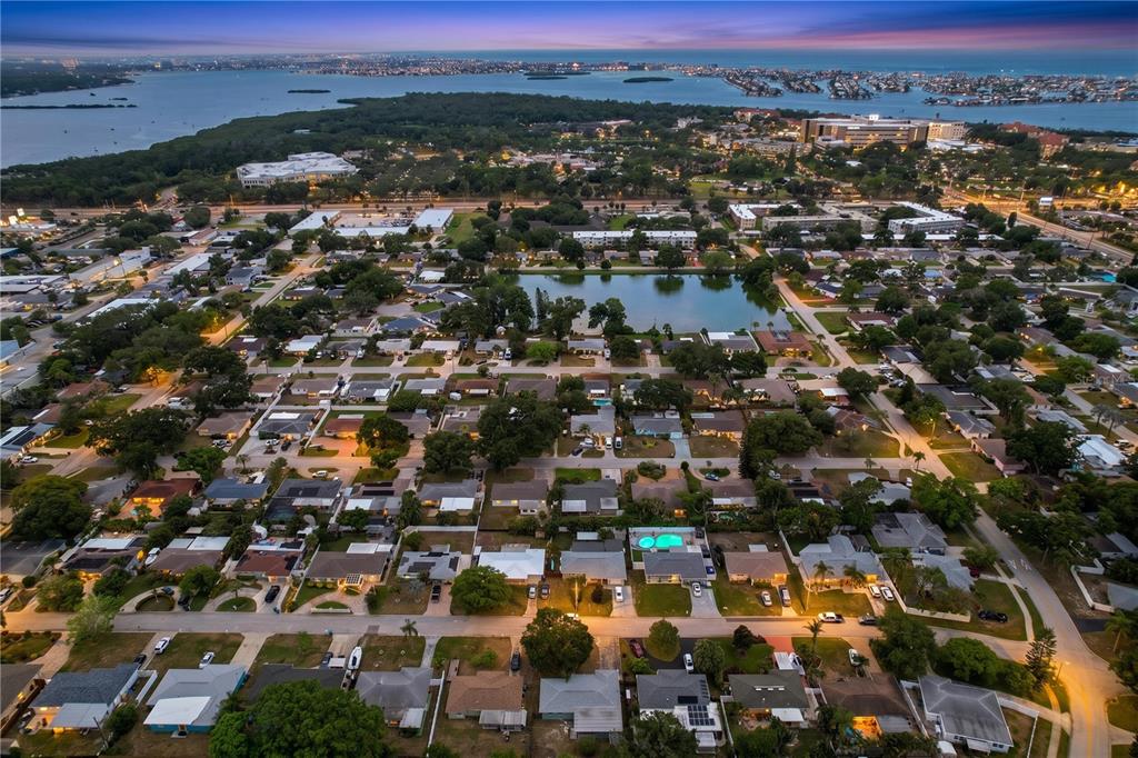 An aerial view of a suburban neighborhood featuring a central pond at twilight — 9813 51ST AVENUE N, ST PETERSBURG, FL