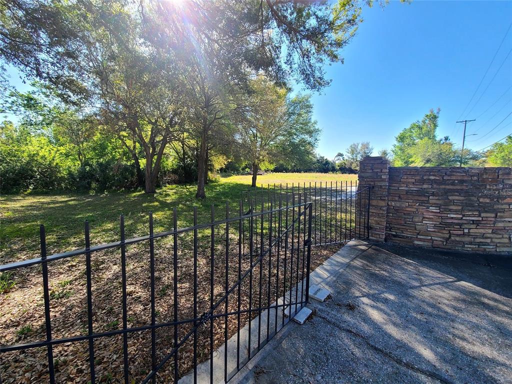 A metal gate opens to a grassy, tree-lined lot next to a stone wall — 3541 N BOULEVARD, TAMPA, FL
