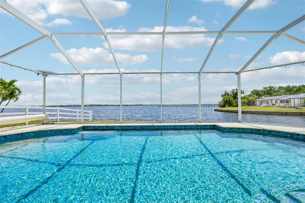 A screened-in swimming pool overlooks a large lake with a white fence and distant houses — 3072 MAUCK TERRACE, PORT CHARLOTTE, FL