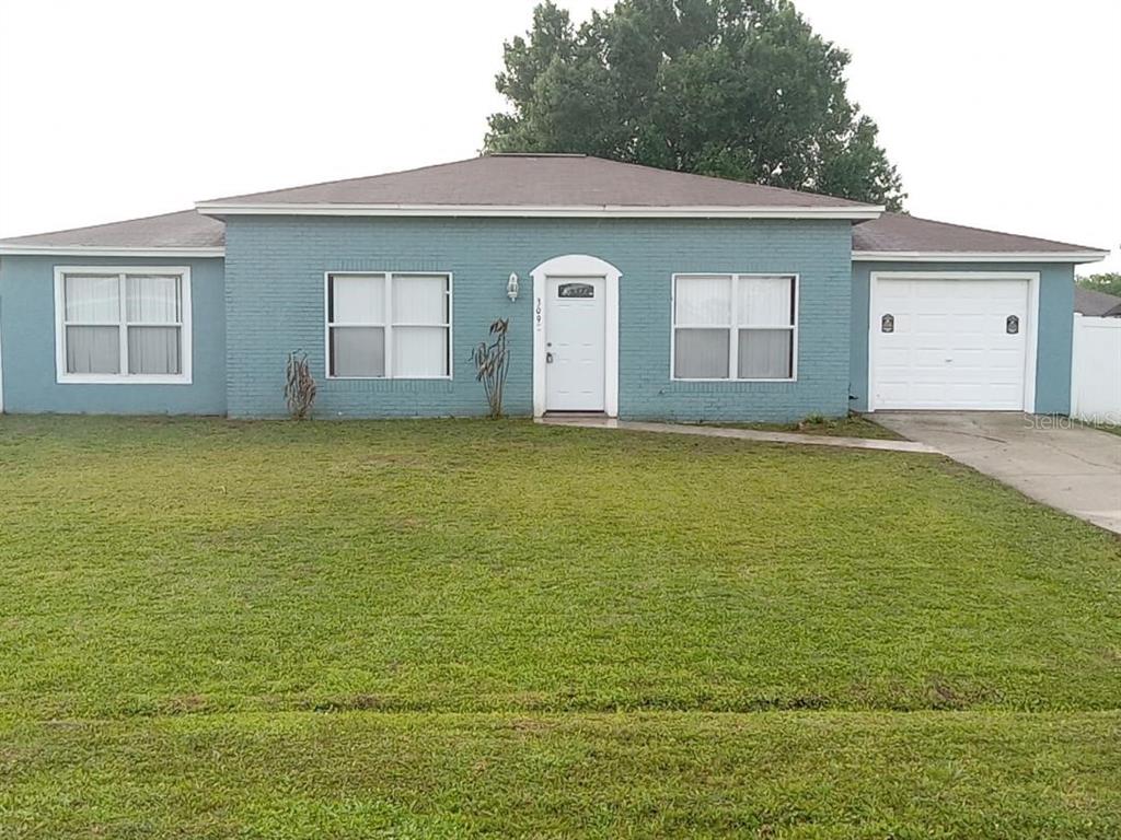A single-story blue brick house features a white front door, garage, and a large lawn — 309 CORNWALLIS COURT, KISSIMMEE, FL