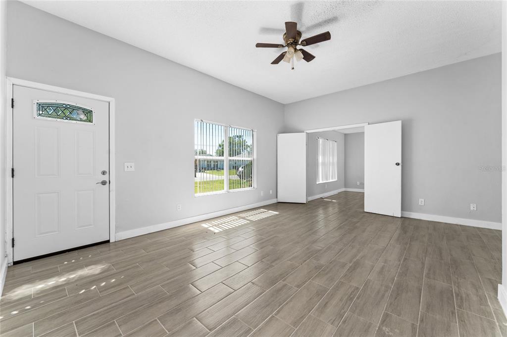 An empty living room features light gray walls, wood-look tile flooring, and a ceiling fan — 309 CORNWALLIS COURT, KISSIMMEE, FL