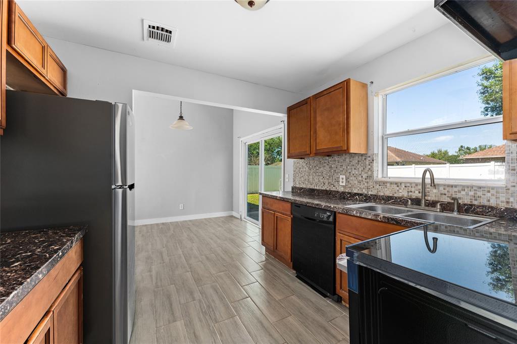 A kitchen with wood cabinets, dark countertops, tile flooring, and a sliding glass door — 309 CORNWALLIS COURT, KISSIMMEE, FL