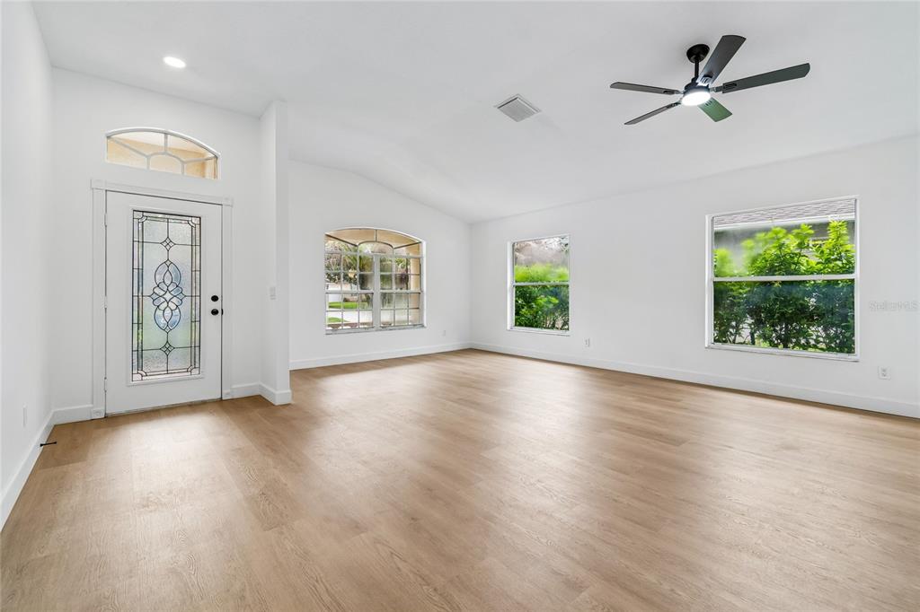 An empty living room features white walls, light wood-look flooring, a ceiling fan, and windows — 3041 BEAVER POND TRAIL, VALRICO, FL