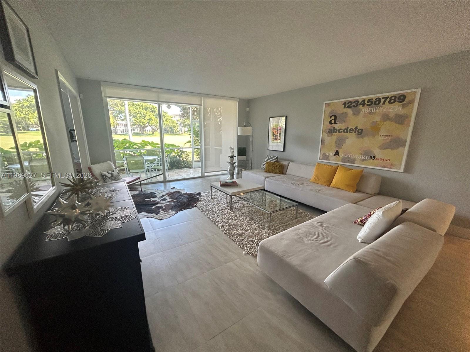 A living room features a large sectional sofa, glass coffee tables, and a sliding glass door — 4017 N Cypress Dr # 102, Pompano Beach FL 33069, POMPANO BEACH, FL