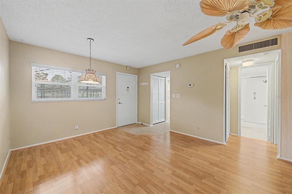 A living area with light wood flooring, a ceiling fan, and a white entry door — 11485 OAKHURST ROAD UNIT 204, LARGO, FL