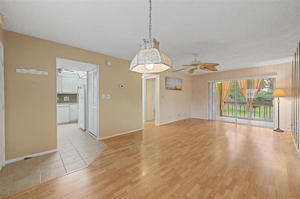 A living room with wood-look flooring, a ceiling fan, a pendant light, and sliding doors — 11485 OAKHURST ROAD UNIT 204, LARGO, FL