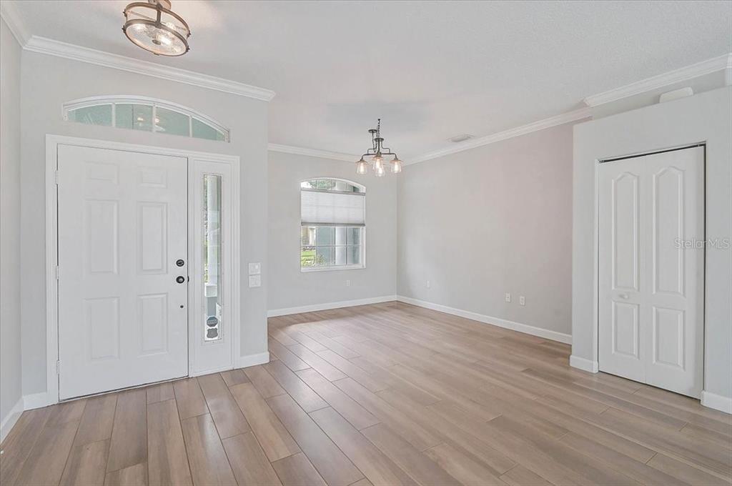 An empty room with light wood flooring, white walls, a front door, and two light fixtures — 10647 OLD GROVE CIRCLE, BRADENTON, FL