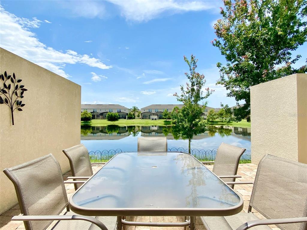 A patio with a glass-top table and chairs overlooks a pond and residential buildings — 3175 TOCOA CIRCLE, KISSIMMEE, FL