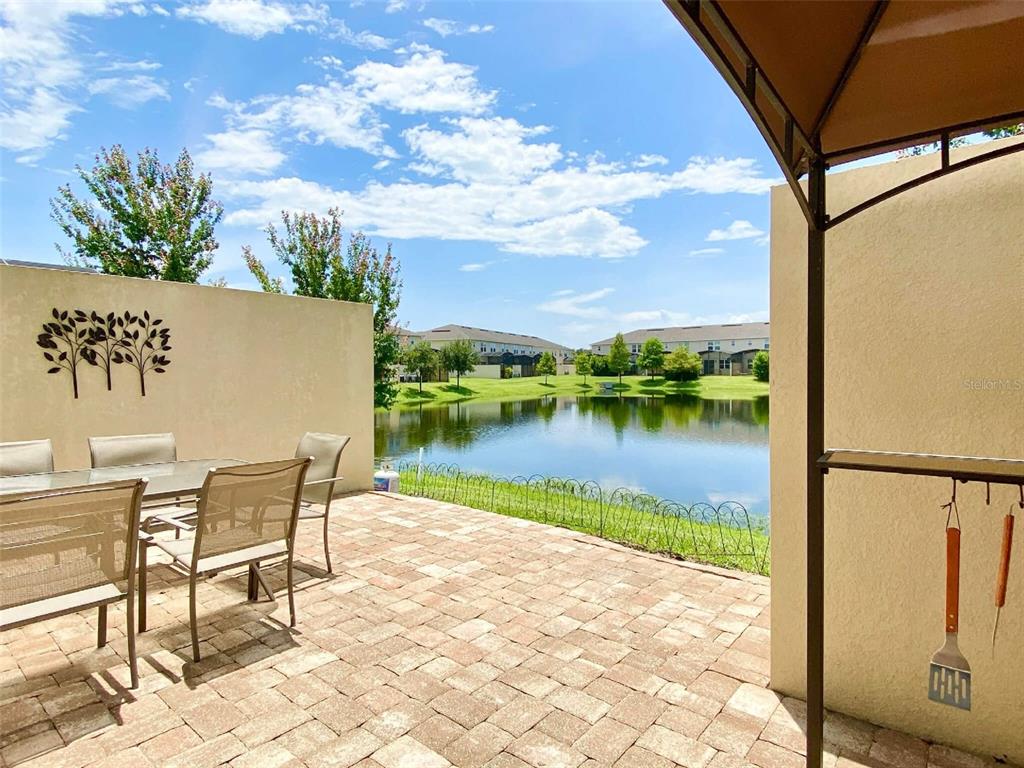 A paved patio with outdoor furniture overlooks a pond and residential buildings under a blue sky — 3175 TOCOA CIRCLE, KISSIMMEE, FL