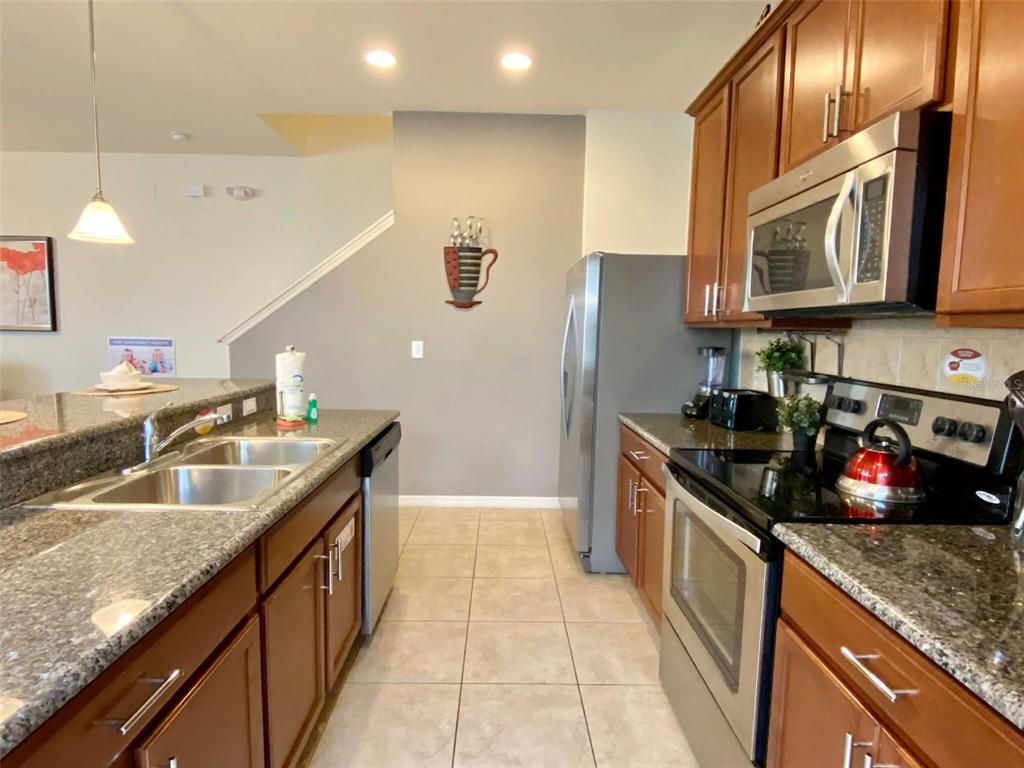 A kitchen features dark wood cabinets, granite countertops, stainless steel appliances, and tile flooring — 3175 TOCOA CIRCLE, KISSIMMEE, FL