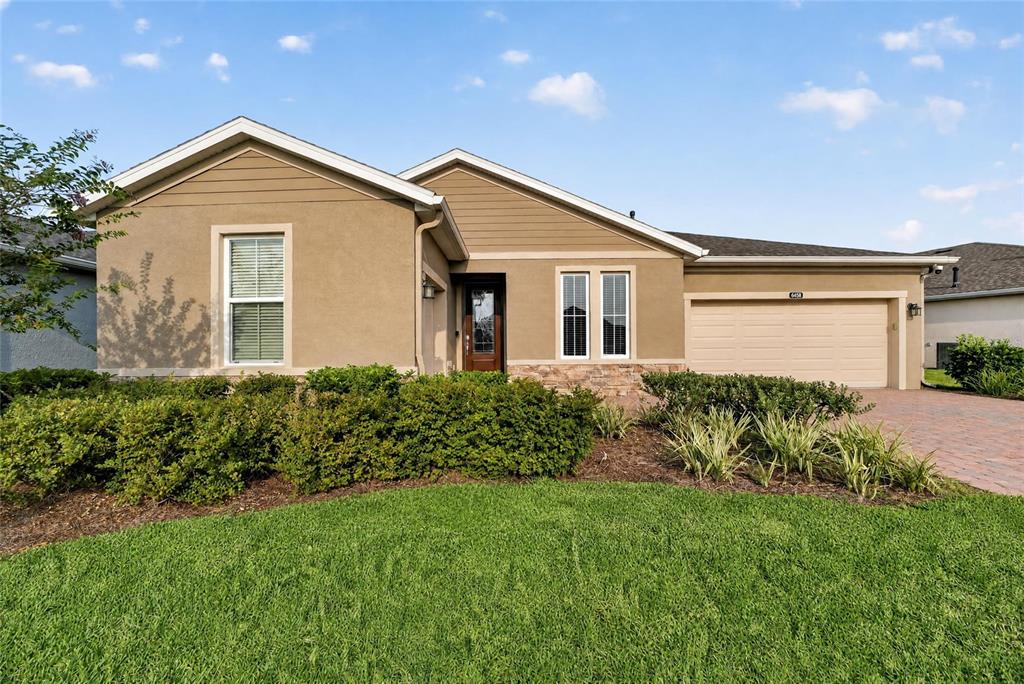 A tan single-story house with a brick paver driveway and a three-car garage — 4436 NW 53RD COURT, OCALA, FL
