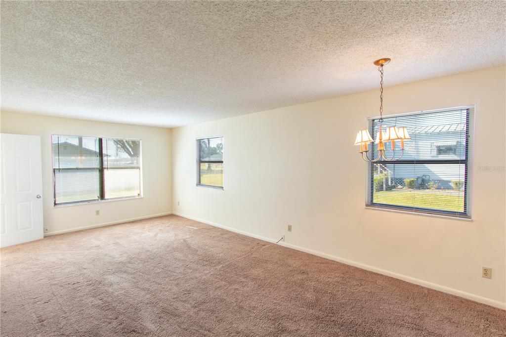 An empty room with beige carpet, white walls, three windows, and a hanging light fixture — 709 MOSLEY ROAD, LAKE ALFRED, FL