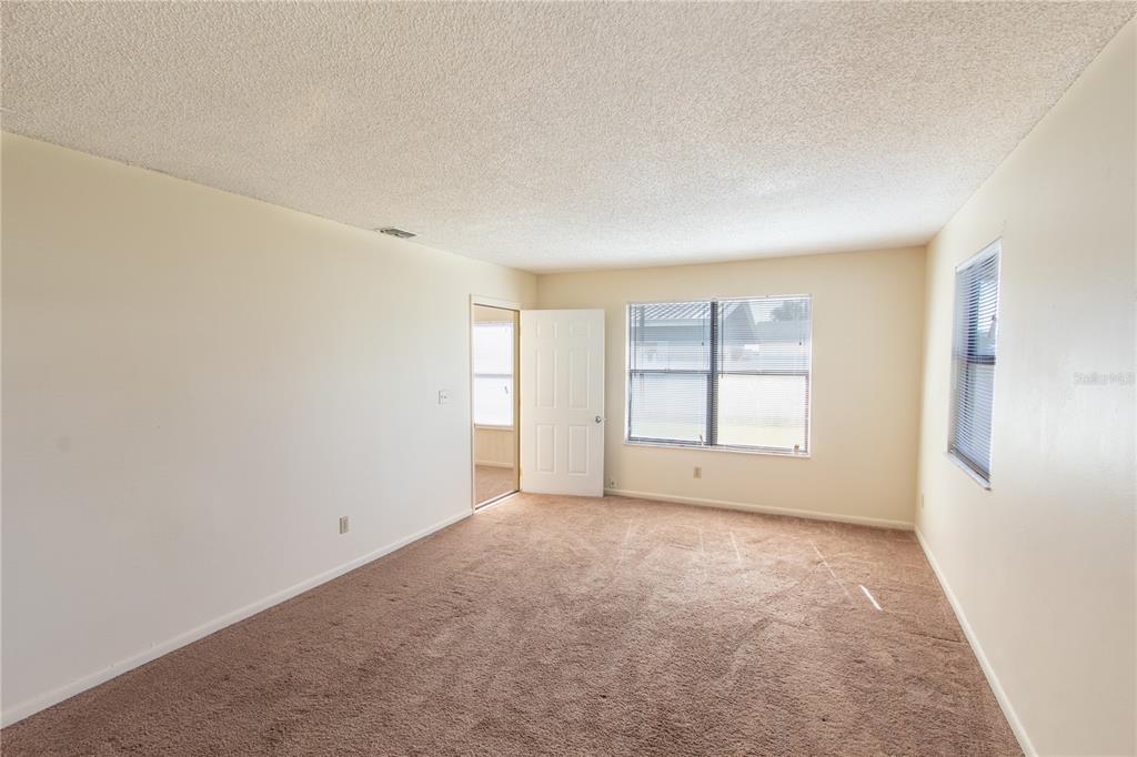 An empty room with beige walls, brown carpeting, and two windows with blinds — 709 MOSLEY ROAD, LAKE ALFRED, FL