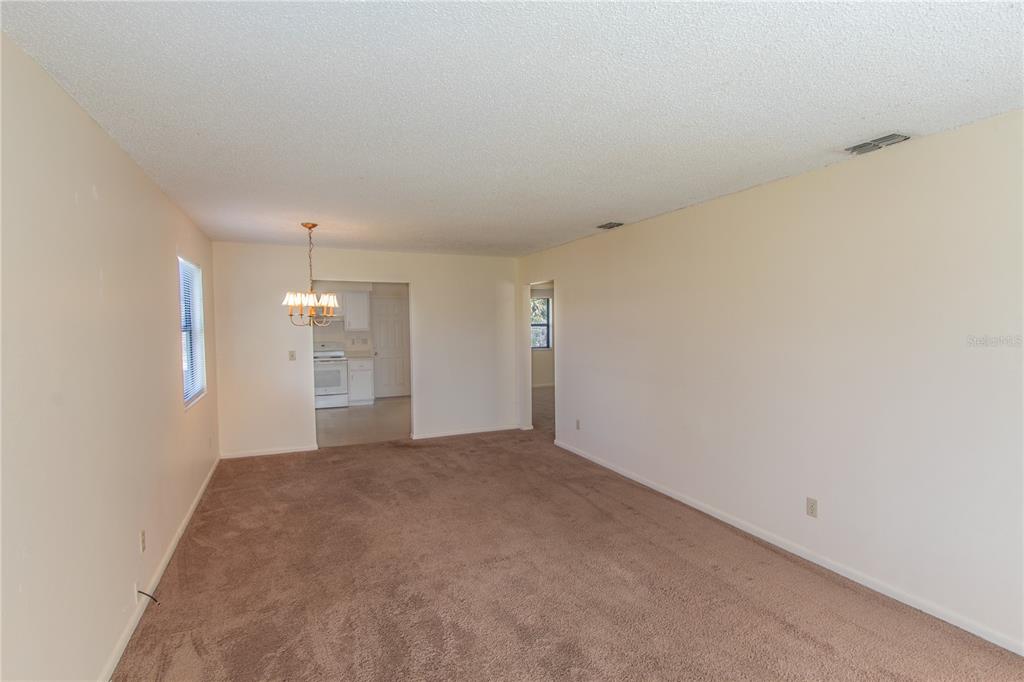 A carpeted living room leads to a dining area with a chandelier and kitchen beyond — 709 MOSLEY ROAD, LAKE ALFRED, FL
