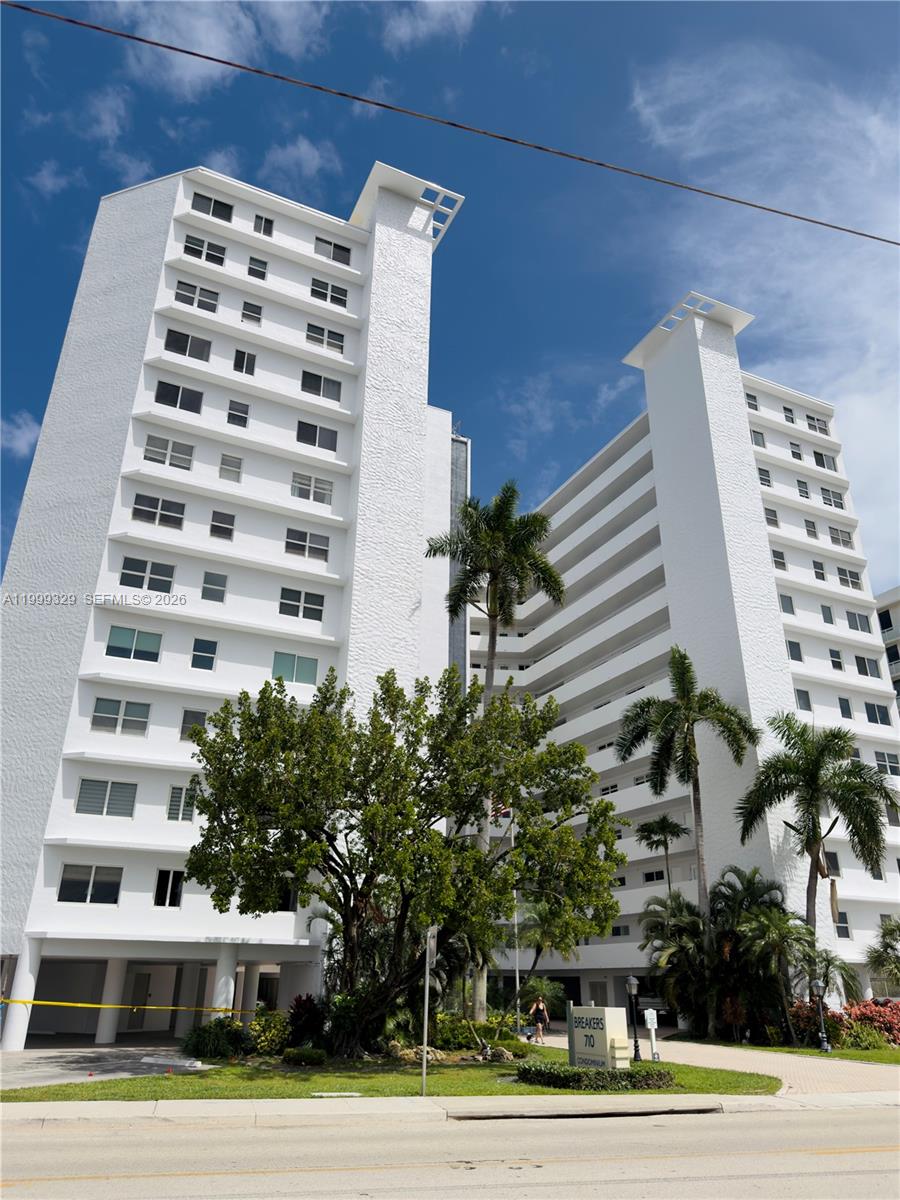 A tall white condominium building features balconies and palm trees in front of the entrance — 710 N Ocean Blvd # 603, Pompano Beach FL 33062, POMPANO BEACH, FL