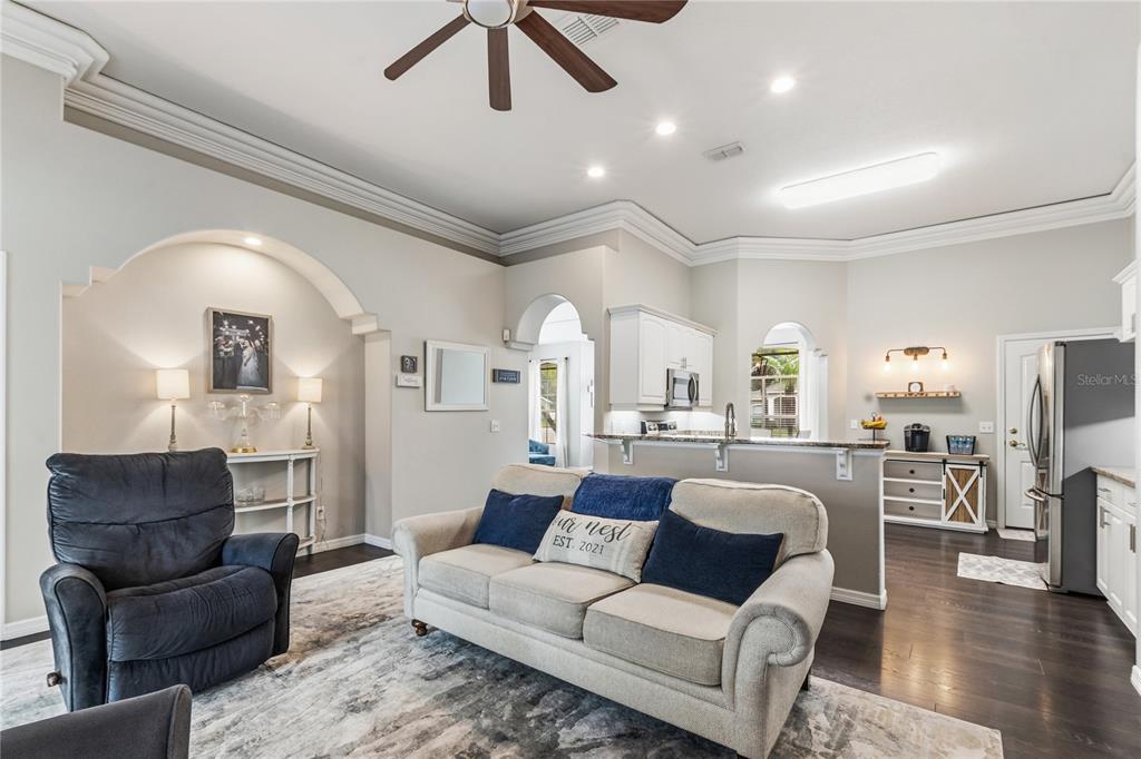 A living room with a beige sofa and dark recliner opens to a kitchen with white cabinets — 1015 ROBIN LANE, WINTER HAVEN, FL